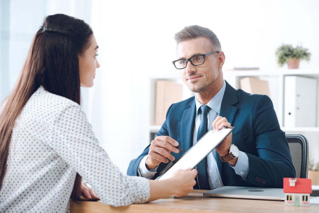 insurance agent pointing at clipboard in clients hand at tabletop in office, house insurance concept
